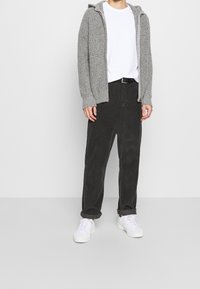 Grå stickad hoodie med ribbat mönster, vit t-shirt med rund hals, svarta sammetsbyxor och vita sneakers, allt bärs avslappnat.