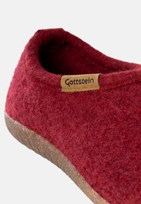 Czerwony filcowy kapcie z teksturowaną górą, naturalną korkową podeszwą oraz małą skórzaną metką z logo "Gottstein". Gładki i miękki wygląd.