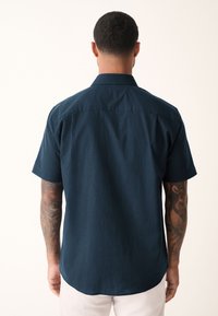 Donkerblauw shirt met korte mouwen, rechte snit, kraag en zichtbare stiksels. Heeft een gladde textuur en een afgeronde zoom.