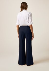Marineblauwe wijde broek met elastische tailleband, gecombineerd met een wit overhemd met kraag, voorzien van opgerolde mouwen en een gestructureerde kraag.