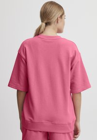 Overdimensioneret rosa sweatshirt med en blød, struktureret finish. Har en ribbet krave og manchetter samt en lige søm med sideslids.