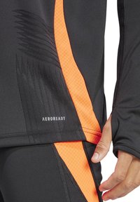 Zwarte sporttop met oranje accenten en textuurpatronen. Inclusief "AEROREADY" merk, ontworpen voor vochtbeheer.