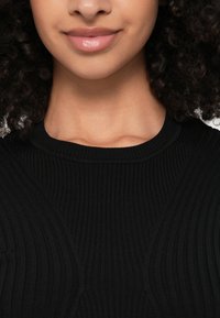 Μαύρο ριμπ πουλόβερ με στρογγυλή λαιμόκοψη και υφή. Κοντινή λήψη των λεπτομερειών του υφάσματος και της εφαρμογής γύρω από τον λαιμό.