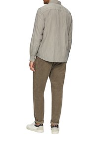 Lichtgrijze button-up shirt met een subtiel textuurpatroon, gecombineerd met een bruine corduroy broek en witte sneakers. Casual fit, opgerolde mouwen.