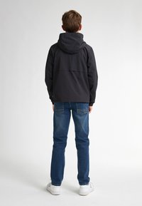 Jachetă neagră cu glugă, cu o croială lejeră, purtată împreună cu blugi din denim albastru. Fundalul este alb uniform, axându-se pe îmbrăcăminte.