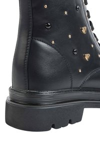Stivale alla caviglia in pelle nera con stud lucidi e dettagli metallici a forma di cuore. Sola in gomma nera spessa con superficie rigata.