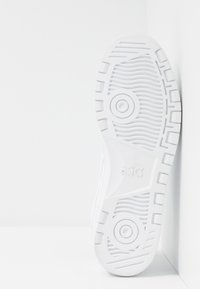 Hvit idrettssko såle med teksturert grep mønster, med sirkulære og lineære design. Logo preget på siden; flat profil.