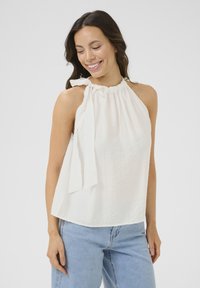 Haut halter blanc avec une finition texturée et un système de laçage au cou, associé à un jean bleu clair. Design simple et décontracté.