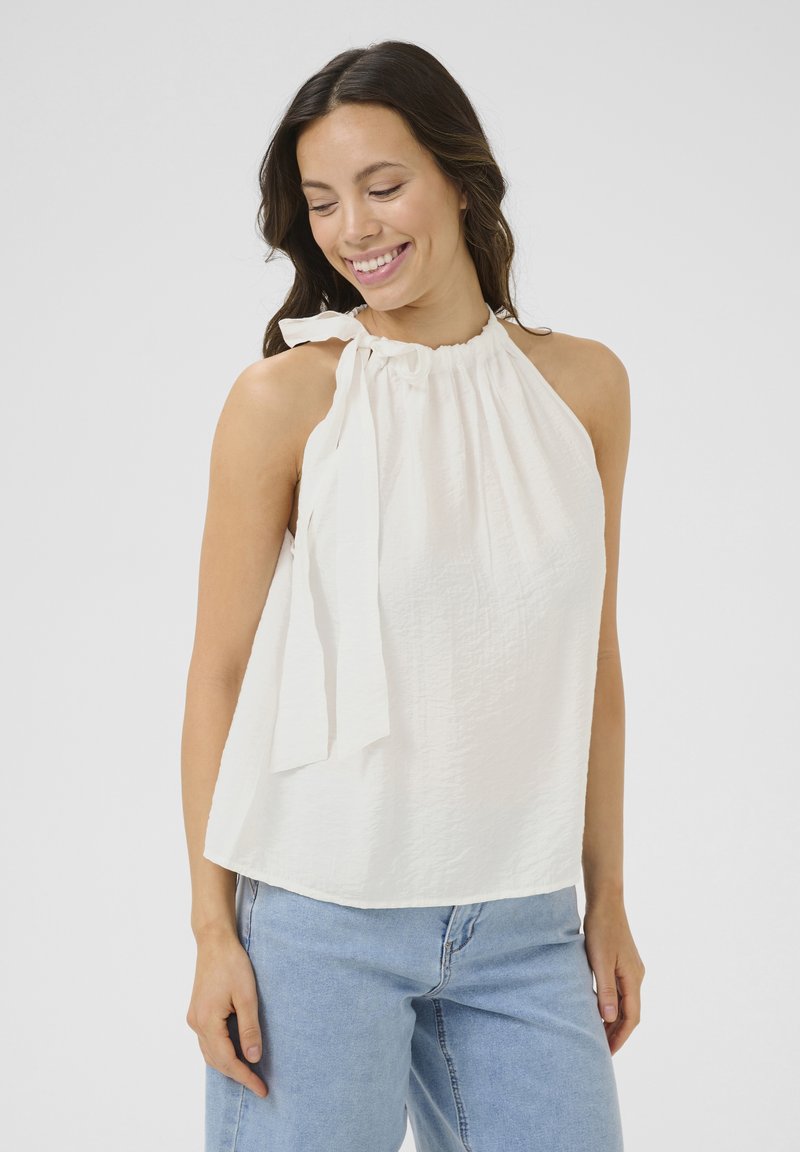 Haut halter blanc avec une finition texturée et un système de laçage au cou, associé à un jean bleu clair. Design simple et décontracté.