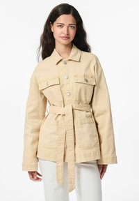 Veste en denim beige avec taille ceinturée, deux poches avant, fermetures à boutons et col. Texture douce, design décontracté.