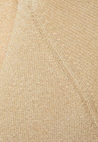 Beige gebreide stof met een gestructureerd oppervlak, voorzien van kleine, gelijkmatig verdeelde gaatjes, wat zorgt voor een lichte en ademende uitstraling.