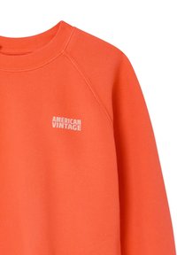 Svijetlo narančasta majica dugih rukava s natpisom "AMERICAN VINTAGE" u bijeloj boji na lijevoj strani prsa, s izrezom u stilu posade i raglan rukavima.
