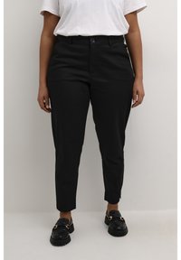 Pantalon noir sur mesure à coupe slim, doté d'une fermeture à bouton, de poches et d'une texture lisse, associé à des mocassins noirs.