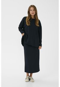 Marineblauwe, losse sweatshirt met lange mouwen en een zak. Gecombineerd met een bijpassende lange rok en lichtgekleurde sneakers.