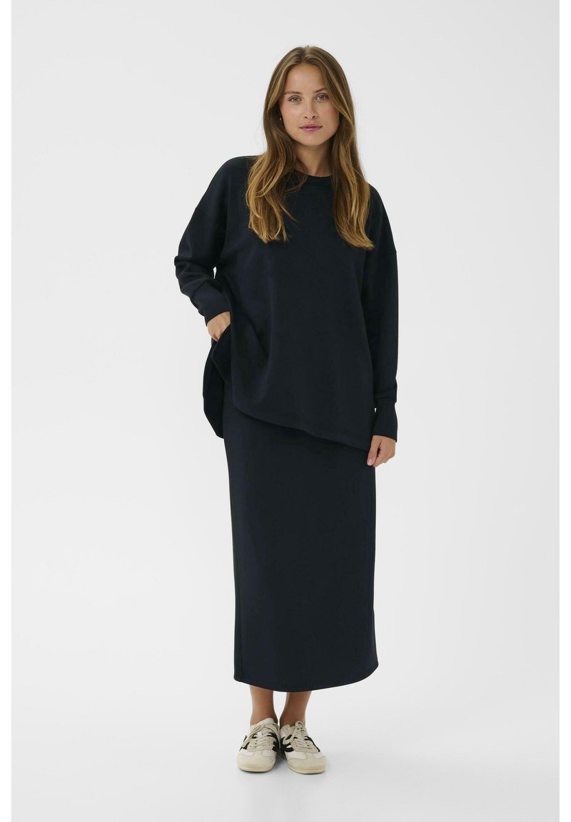 Marineblauwe, losse sweatshirt met lange mouwen en een zak. Gecombineerd met een bijpassende lange rok en lichtgekleurde sneakers.