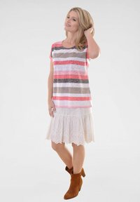 T-shirt à rayures roses, grises et blanches à manches courtes, associé à une jupe blanche en broderie anglaise avec un ourlet volant, complété par des bottines brunes à la cheville.