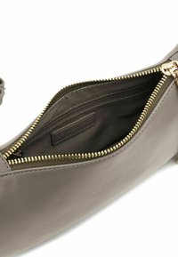 Borsa in pelle grigia con texture liscia, dotata di cerniera dorata e fodera interna in tessuto scuro. L'interno contiene un'etichetta e una tasca pratica.