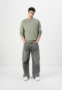 Svetlozelený crewneck sweatshir, šedé široké nohavice a biele tenisky. Jednoduchý dizajn s rebrovanými manžetami a bočnými vreckami.
