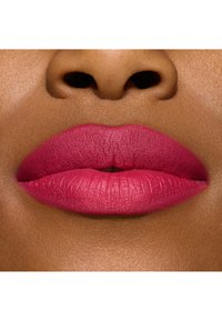 Matte fuksia leppestift på fyldige lepper med en glatt tekstur, satt mot en dyp brun hudtone, som fremhever definerte leppekonturer.