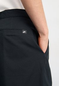 Černé šortky Nike s hladkým povrchem, které mají zadní kapsu a malou značkovou visačku na pasu. Design je minimalistický.