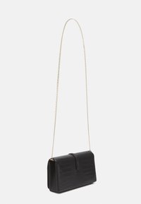 Černá kabelka z krokodýlí kůže s embosovaným vzorem a strukturovaným tvarem. Obsahuje dlouhý zlatý řetízkový popruh. Klopové zavírání na vrcholu, minimální hardware.