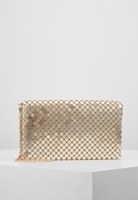 P cartera de metal dorado con patrón hexagonal, superficie brillante y correa de cadena. Forma rectangular plana, textura suave y cierre de cremallera.