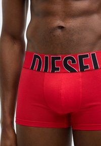 Červené boxerky z mäkkej látky, s širokým čiernym pásom s bielym logom "DIESEL", priliehavý strih s hladkou textúrou.