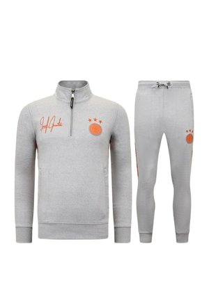 Lichtgrijs sportief trainingspak met een sweatshirt met een kwart ritssluiting en een broek met koord, met oranje logo's en tekst op beide delen.