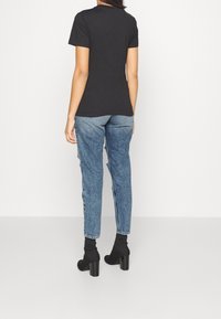 Svart kortärmad T-shirt i kombination med blå denimjeans med avslappnad passform och slitna detaljer, i sällskap med svarta klackade ankelskor.