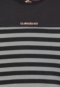 Stripete T-skjorte i svart og grått med rund hals og en liten rosa Quiksilver-logo på brystet. Laget av myk bomullsmateriale.