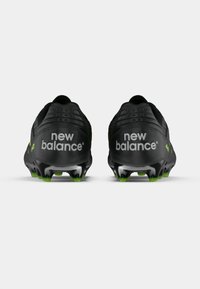 Černé fotbalové kopačky se zelenými akcenty; mají texturovaný povrch a výrazné logo "new balance" na patě.