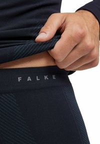Leggings thermiques noirs avec une finition texturée et un motif de rayures diagonales. La taille affiche le nom de la marque "FALKE" de manière proéminente.