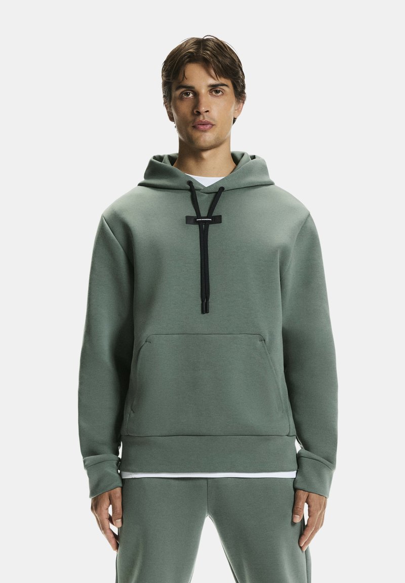 Laza zöld kapucnis pulóver, puha anyagból készült. Elöl zsebbel, fekete húzózsinórral és minimalista designnal rendelkezik.