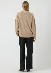 Beżowy we�łniany sweter z prążkowanymi mankietami i dołem, zestawiony z czarnymi spodniami typu wide-leg. Sweter ma okrągły dekolt i teksturowany materiał.