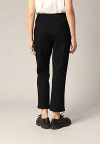 Zwarte broek met elastische taille, rechte snit, met twee achterzakken, op enkellengte, gecombineerd met zwarte veterschoenen.