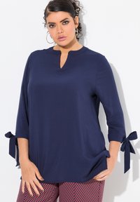 Blusa blu navy con colletto alla mandarino, maniche a tre quarti e dettagli con fiocco ai polsini; tessuto morbido con una vestibilità comoda.