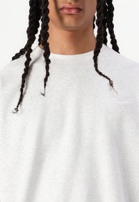 Lys grå sweatshirt lavet af fleece materiale, med crew neck, subtil Nike-logo på brystet, og synlig tekstur.