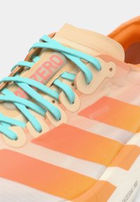 Close-up of a sneaker featuring orange and pink stripes, blue laces, and a visible logo on the side. The sole is white with text.