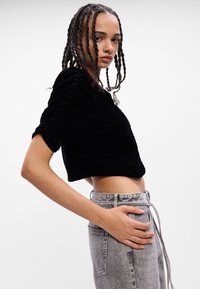 Top cropped in velluto nero con maniche a sbuffo, abbinato a jeans in denim grigio a vita alta con tasche e dettaglio con cordoncino.