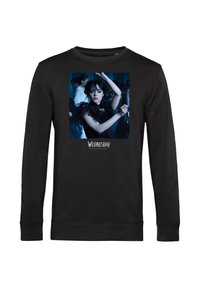 Zwart langslavende shirt met een afbeelding van een vrouw met donker haar in een zwarte jurk die danst, met de tekst "Woensdag" onder de afbeelding.