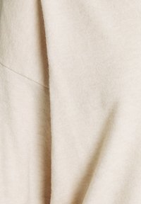 Tissu en maille doux beige avec une surface légèrement texturée. Le matériau est drapé, affichant une forme fluide et lisse avec de doux plis.