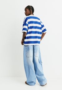 Blau-weißer gestreifter übergroßer T-Shirt mit kurzen Ärmeln, kombiniert mit hellblauen weit geschnittenen Jeans aus Denim mit Taschen und einem ausgefransten Saum.
