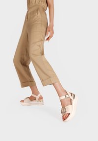 Sandali platform beige con una vasta fascia, dettaglio con fibbia e tacco traslucido. Abbinati a pantaloni croppati in khaki chiaro.