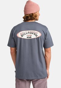 Camiseta de manga corta gris con un gran logo circular de Billabong en rosa y negro en la parte posterior. Tejido suave con un ajuste estándar.