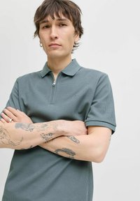 Pique polo shirt in een gedempt groen, met een ritskraag en korte mouwen. Getextureerde stof en subtiele logo detail op de borst.
