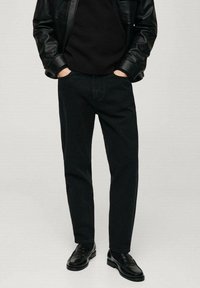 Vaqueros de mezclilla negra con corte recto, que cuentan con un diseño clásico de cinco bolsillos y costuras sutiles, combinados con una chaqueta de cuero negra.