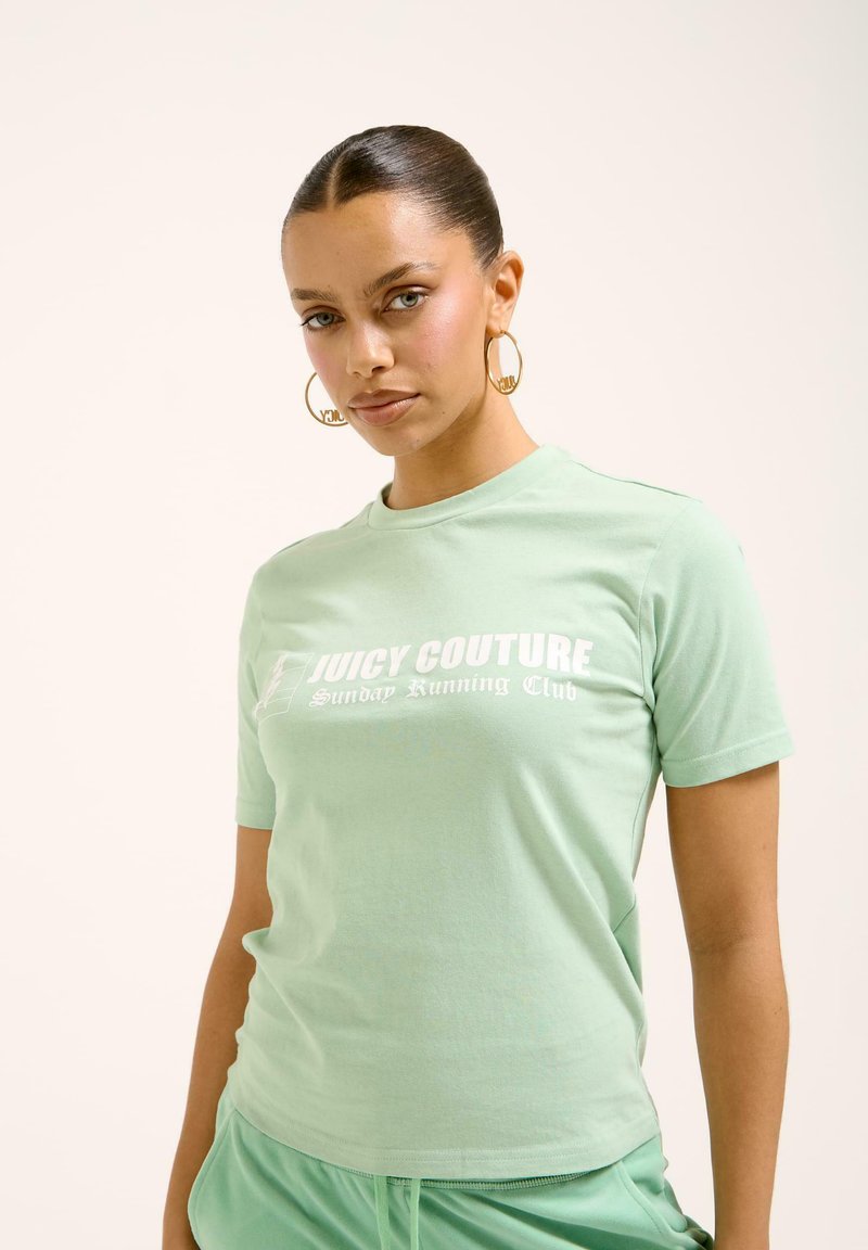 Šviesiai žalia medvilninė marškinėliai su balta spauda, kuriuose užrašyta "Juicy Couture Sunday Running Club". Pusiau prigludusi forma, su apvalia iškirpte ir trumpomis rankovėmis.
