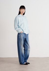 Lys blå skjorte med lange ermer, parret med løstsittende, slitte blå jeans. Enkelt design med avslappet silhuett.