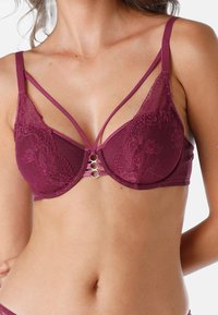 Bralette in pizzo bordeaux con design a pois, caratterizzato da uno stile con bretelle e anelli metallici argentati al centro per un tocco di dettaglio.