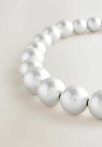 Okrogle srebrne perle z gladko, sijočo površino, razporejene v neprekinjeni vrsti, ki prikazujejo različno velikost in odsevno teksturo.